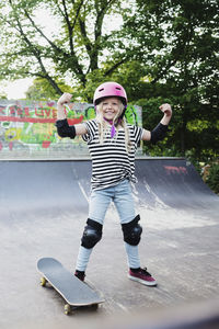 Smiling girl flexing muscles while standing on skateboard ramp