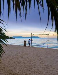 People at beach against sky during sunset