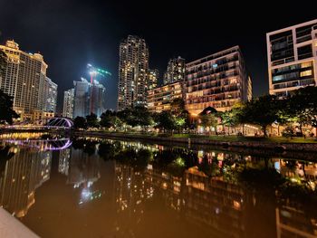 Illuminated buildings by river against sky at night