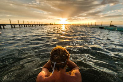 Rear view of shirtless man against sea during sunset