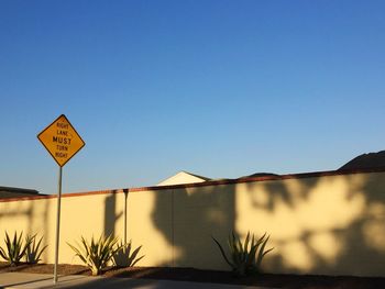 Road sign on footpath by wall against clear blue sky