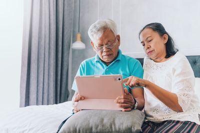 Senior couple using digital tablet while sitting on bed