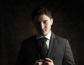 Portrait of young man standing against black background