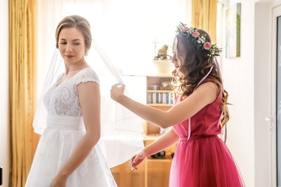 Side view of woman assisting bride getting dressed at home