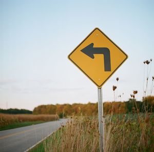 Arrow sign on field by road against clear sky