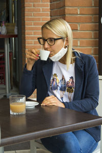 Young woman with mask pulled down drinking coffee cup