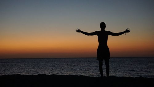Silhouette man standing on shore at beach during sunset