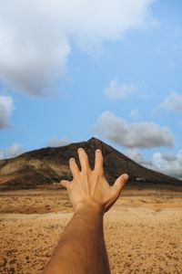 Cropped hand of man gesturing against mountain and sky