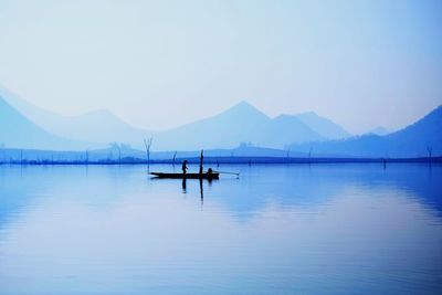 Silhouette person in boat on lake against sky