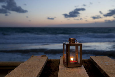 Close-up of illuminated candle on table against sea against dusk