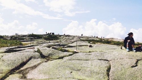 Rear view of woman standing on rock against cloudy sky