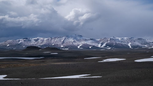 Scenic view of landscape and snowcapped mountains against cloudy sky