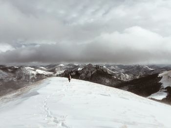 Man walking on snow covered mountain against sky