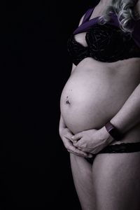 Midsection of woman touching hair over black background