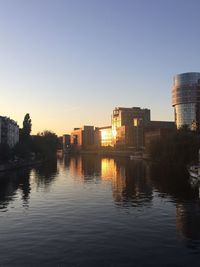 Buildings by river against clear sky at sunset