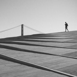 Man walking on suspension bridge against clear sky