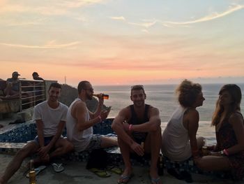 Friends enjoying on beach against sky during sunset