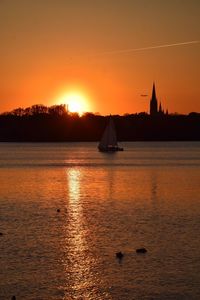 Silhouette sailboats in sea against orange sky