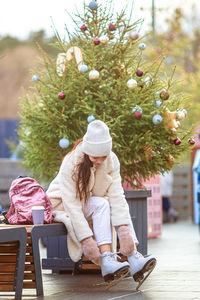 Full length of woman sitting by christmas tree