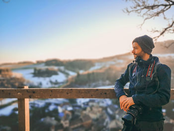 Young man looking at railing against sky