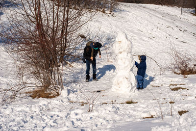 Father playing with children around snowman. fun in the park.