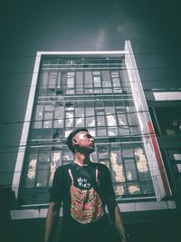 Low angle view of young woman looking away against building