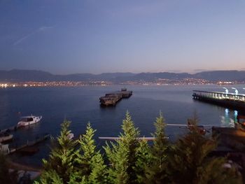 Illuminated cityscape by sea against clear sky at night