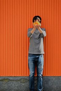 Full length of boy eating food against orange wall