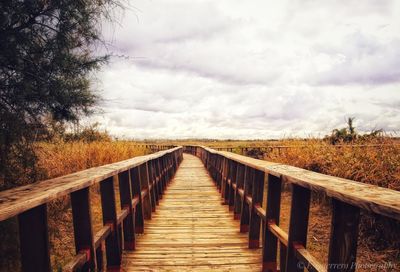 View of wooden footbridge on land against sky