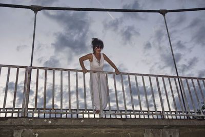 Low angle view of senior woman standing by railing against sky