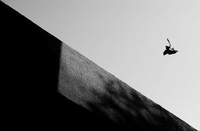 Low angle view of pigeon flying by wall against clear sky