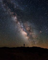 Silhouette person standing on landscape against star field at night