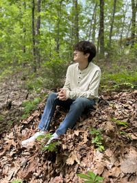 Side view of young woman sitting in forest