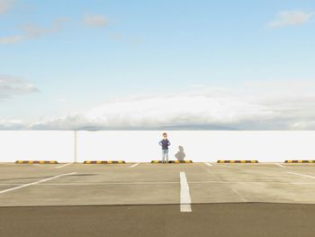 Full length of boy standing by wall against cloudy sky