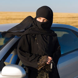 Woman wearing hijab standing by car