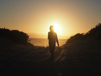 Silhouette woman walking on sand against beach during sunset