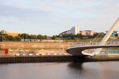 Bridge over river by buildings in city against sky