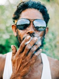 Close-up portrait of man in sunglasses smoking cigarette outdoors