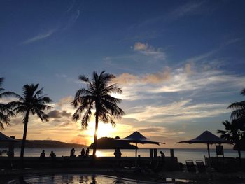 Tourists silhouetted against sunset overlooking sea at resort