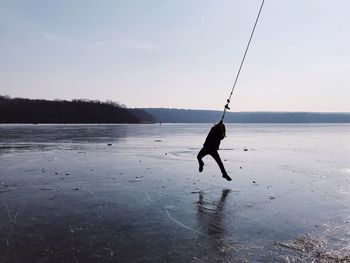 Silhouette of a boy swinging out over the ice on a frozen lake during winter