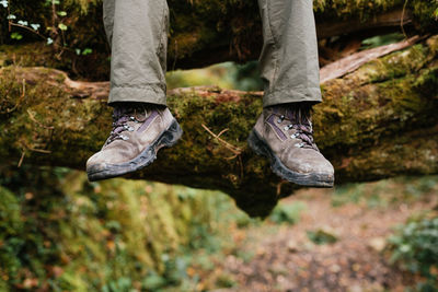 Legs of crop explorer in trekking boots sitting on mossy ground in forest during summer adventure