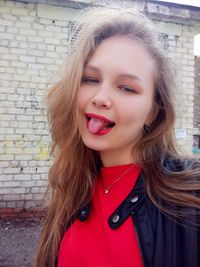 Portrait of beautiful woman sticking out tongue while standing against brick wall