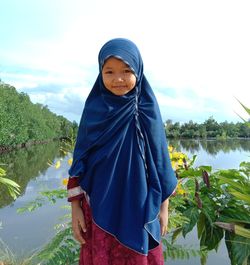 Portrait of smiling girl wearing hijab standing against lake