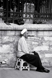 Side view of man sitting on seat against wall