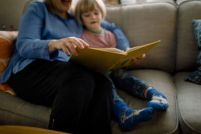 Grandmother reading storybook for grandson while sitting on sofa at home