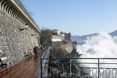 People on railing by sea against clear sky