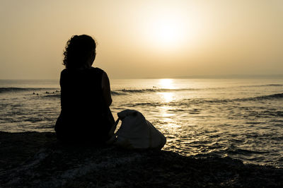 Rear view of woman sitting on beach against sky during sunset