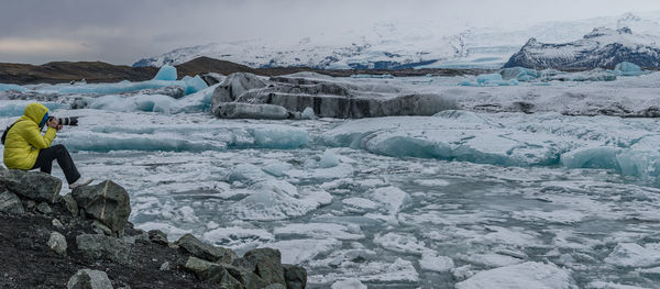 A photographer takes in a panoramic view of blue glacier ice floating in a lagoon