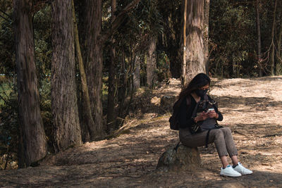 Full length of man sitting on tree trunk in forest