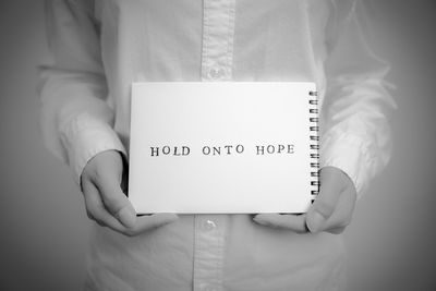 Midsection of person holding text on notepad against white background